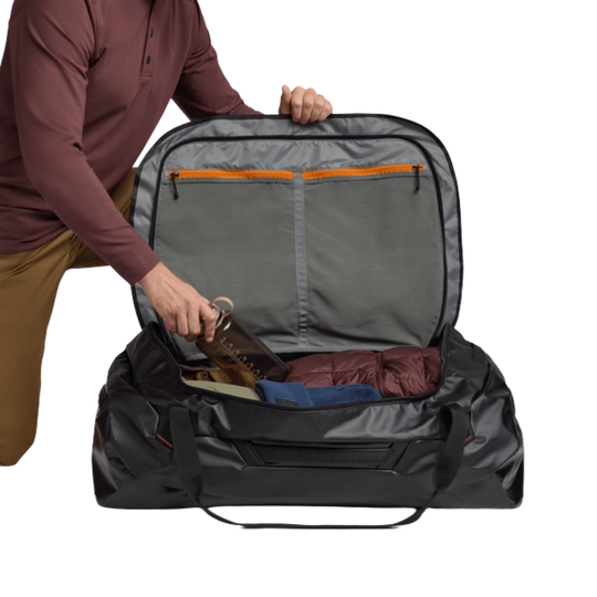 Person packing a large gray duffel bag with various items on a white background