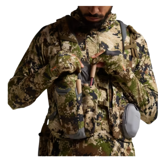 Person wearing a camouflage jacket with various pockets and pouches on a white background