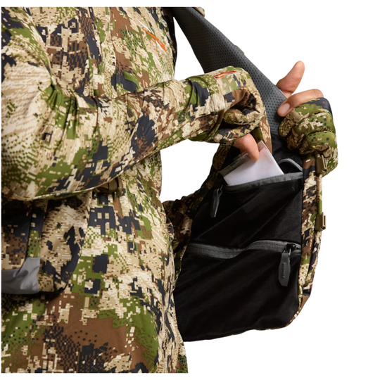 Person wearing camouflage gear holding a black bag with a white label.