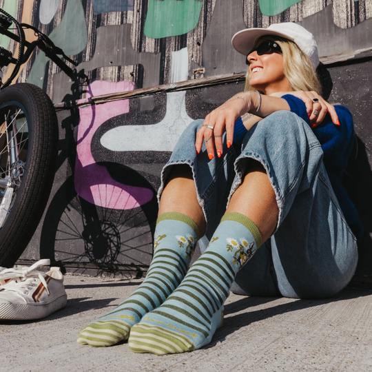 Woman sitting on the ground wearing striped socks with a colorful mural and bicycle in the background