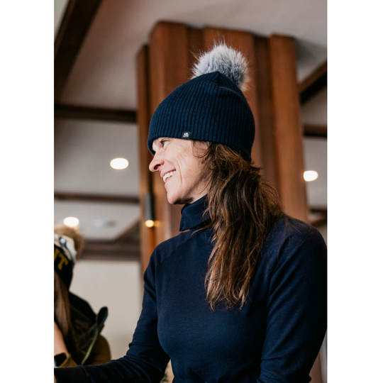 Person wearing a navy beanie with a gray pom-pom indoors.