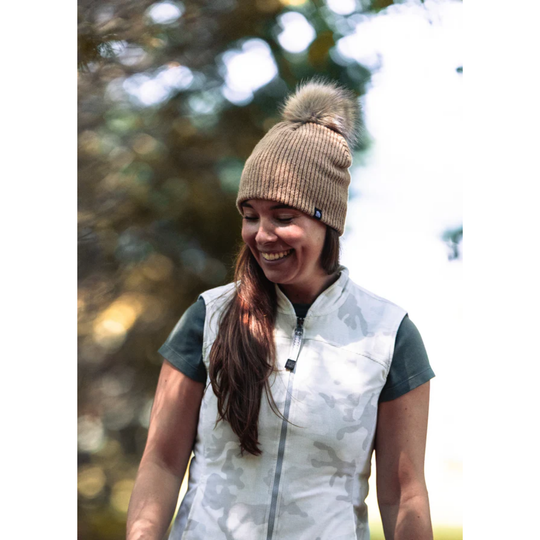 Woman wearing a beanie and outdoor vest with trees in the background