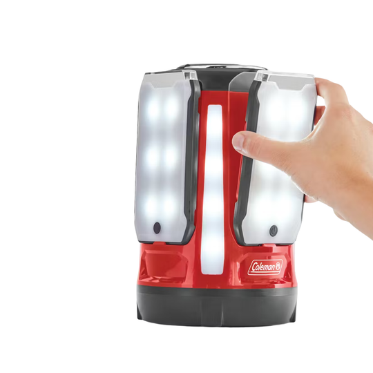 Red and black Coleman lantern held by a hand on a white background