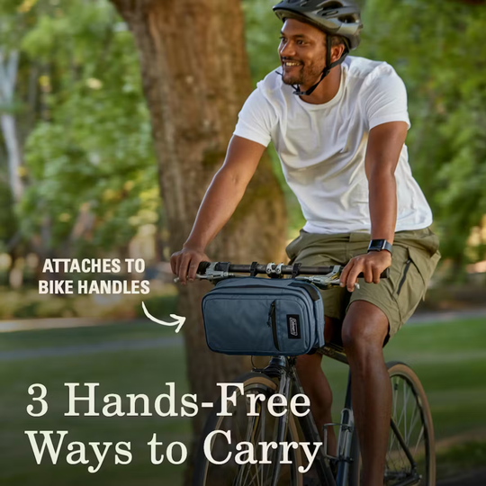 Man riding a bike with a backpack attached to the handlebars, surrounded by greenery.