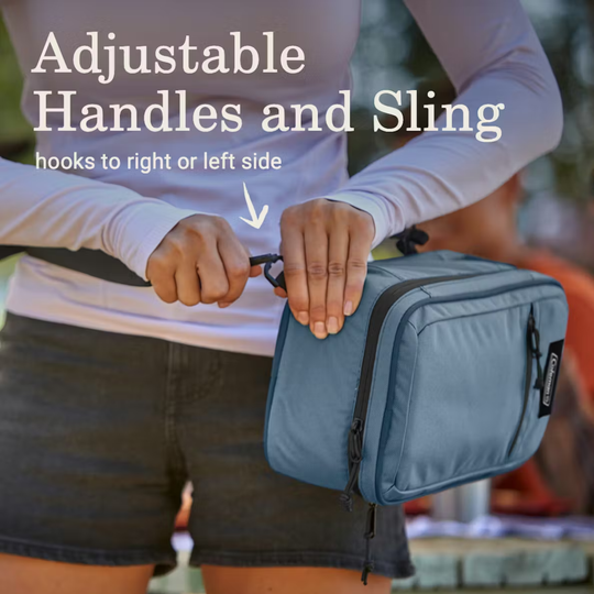 Person holding a blue toiletry bag with adjustable handles and sling feature.