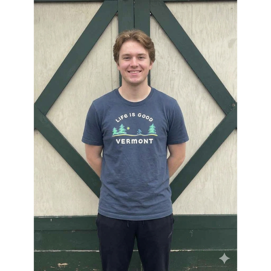 Person wearing a 'Life is Good Vermont' t-shirt standing in front of a wooden background