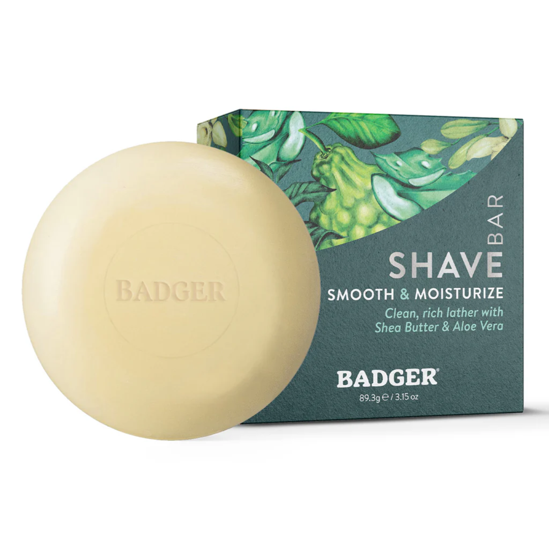 Round beige shave soap bar in front of a teal box labeled SHAVE BAR and SMOOTH & MOISTURIZE
