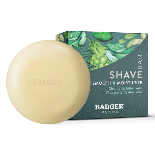Round beige shave soap bar in front of a teal box labeled SHAVE BAR and SMOOTH & MOISTURIZE