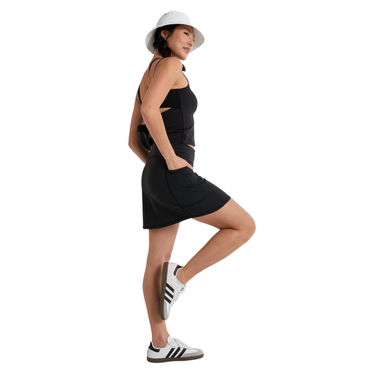 Woman wearing a black dress, white hat, and Adidas shoes on a white background