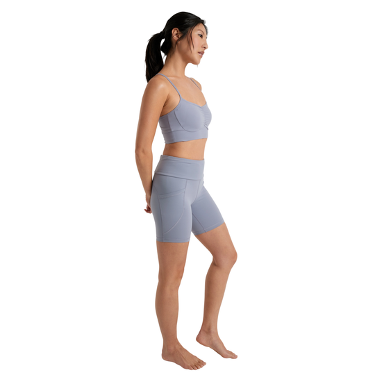 Woman wearing a light gray sports bra and shorts on a white background