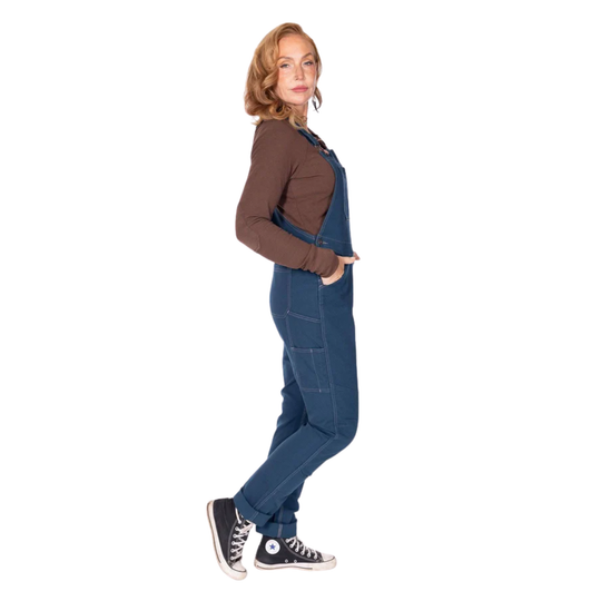 Side view of blue denim overalls worn over a brown long-sleeve top with black high-top sneakers