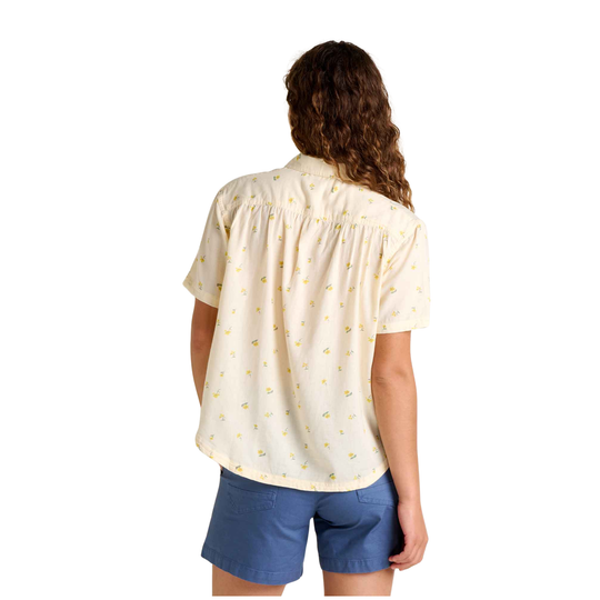 Woman wearing a light-colored blouse with a subtle pattern and blue shorts on a white background