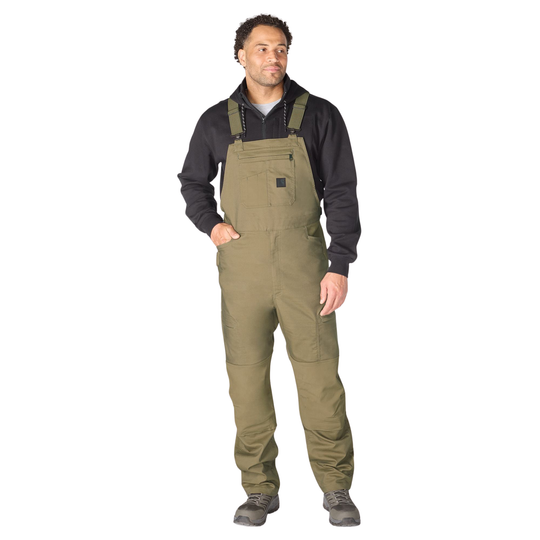 Man wearing a black shirt and green bib overalls on a white background