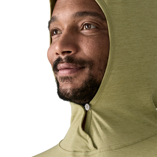 Man wearing a green hooded garment with a neutral background