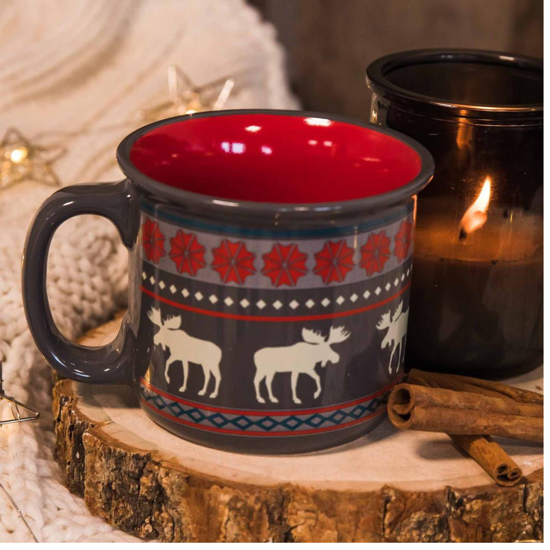 Mug with moose design on a wooden surface with candles in the background