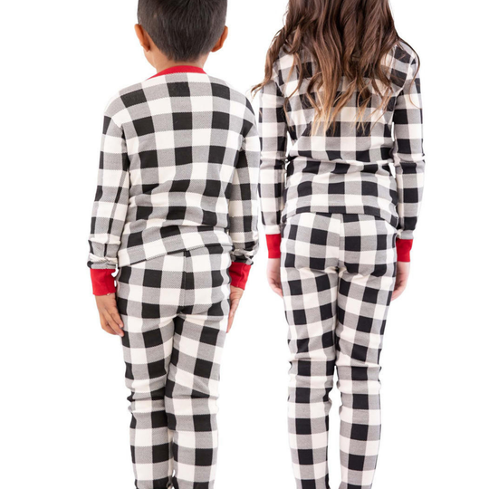 Two children wearing black and white checkered pajamas with red cuffs and trim on a white background.