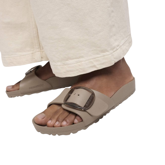 Beige sandals worn with white pants on a white background
