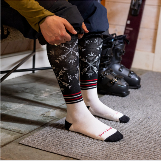 Person wearing patterned leggings and white socks with black accents, standing on a doormat.
