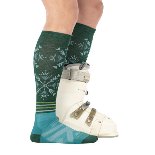 Person wearing green patterned socks with a white ski boot on a white background