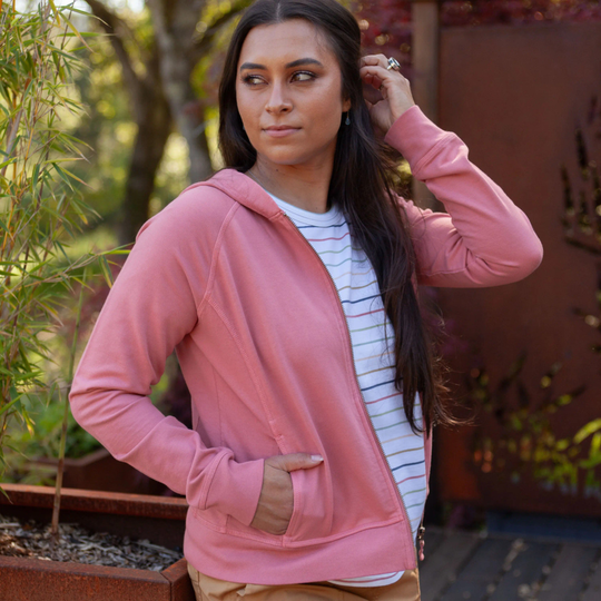 Woman wearing a pink hoodie outdoors with plants in the background