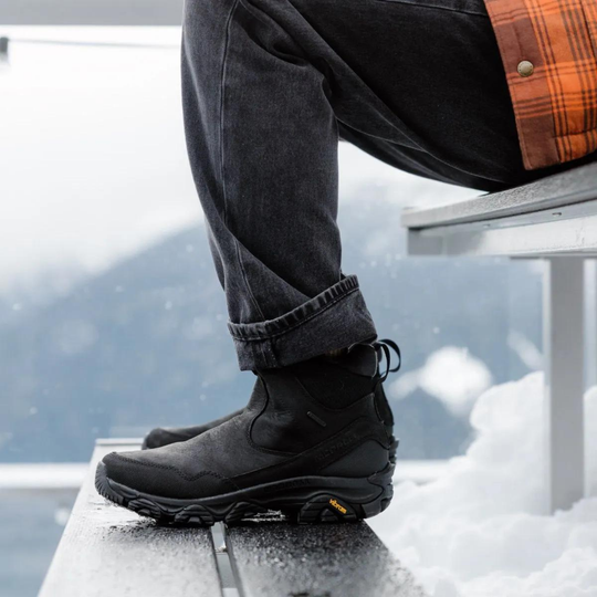 Person wearing black boots and dark jeans sitting on a snowy surface.