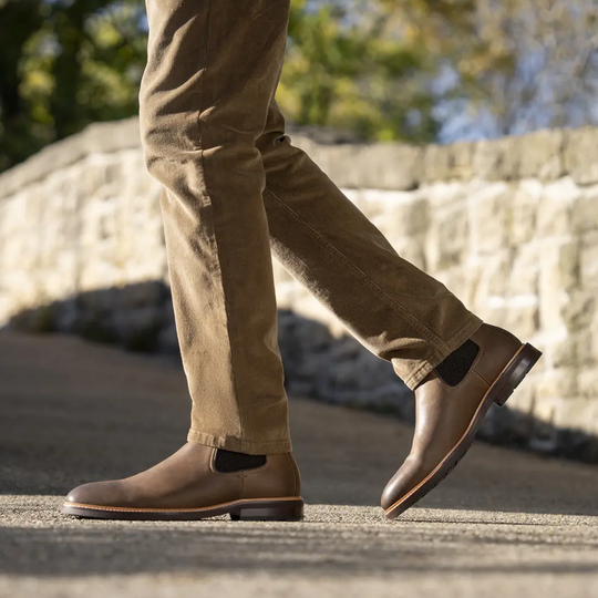 Brown leather boots and beige pants on a stone surface with blurred natural background