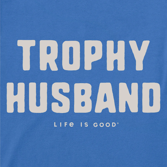 Blue t-shirt with 'Trophy Husband' text and 'Life is Good' logo on a blue background