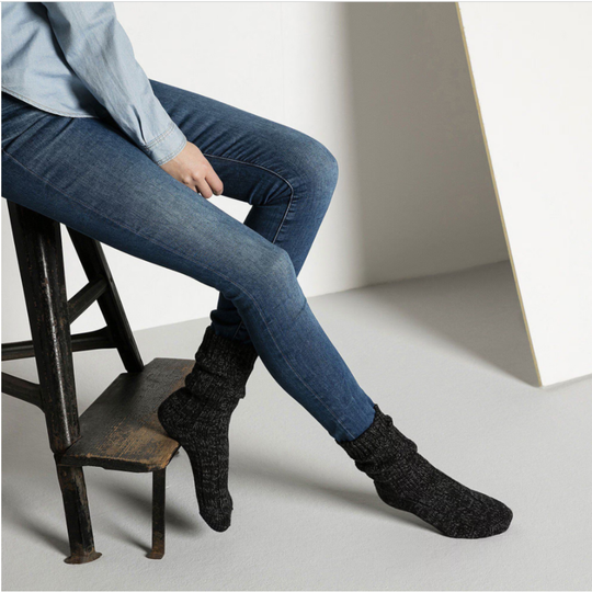 Person wearing blue jeans and black socks sitting on a wooden stool.