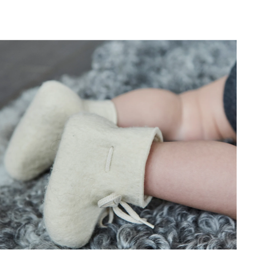 Baby's feet wearing cream-colored booties on a soft gray surface