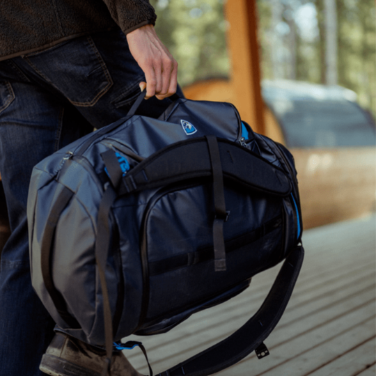Person holding a blue duffel bag with blue accents outdoors.