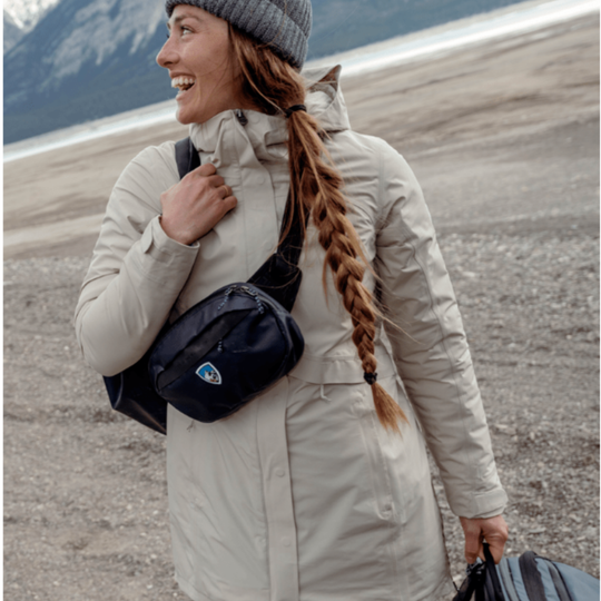 Woman with a waist pack in a snowy landscape wearing a coat and carrying a bag.