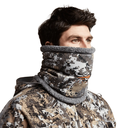 Person wearing a camouflage jacket and gray neck gaiter on a white background
