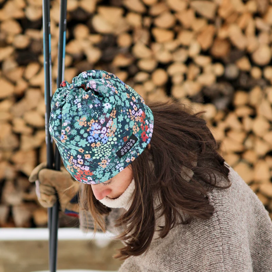 Person wearing a floral beanie in front of stacked firewood