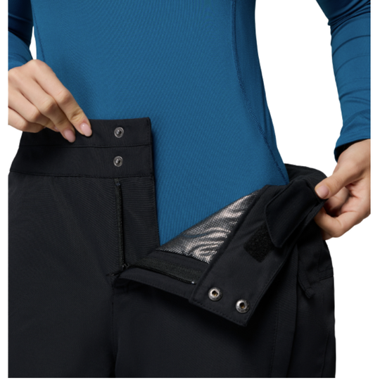 Woman wearing Columbia Women's Bugaboo III Snow Pants - Black on white background. zoomed in showing button snap closure with zipper