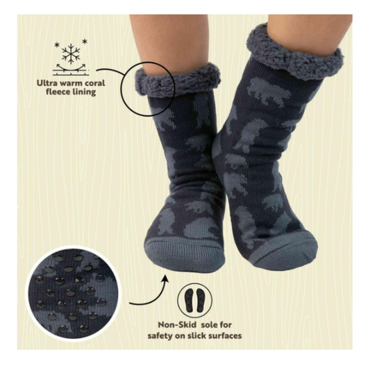 A pair of dark navy socks with a gray bear pattern, featuring a thick gray fleece trim at the top. The image includes text callouts highlighting 'Ultra warm coral fleece lining' and a 'Non-Skid sole for safety on slick surfaces', along with circular detail insets showing the fleece texture and the non-slip sole pattern.