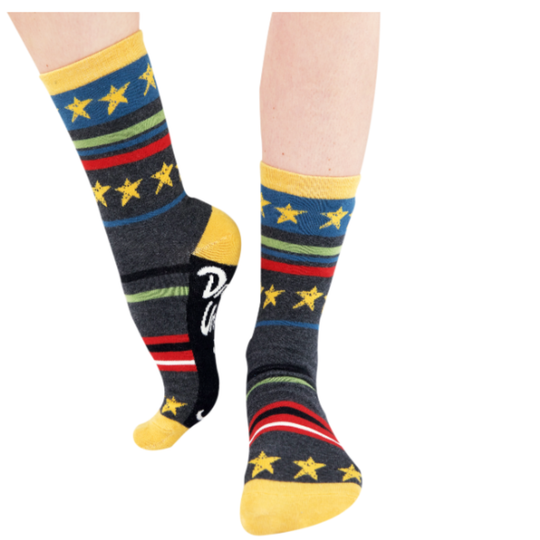 A pair of crew socks worn on feet, featuring a dark gray base with yellow stars, blue, green, and red stripes, and a black heel section with a white script logo.
