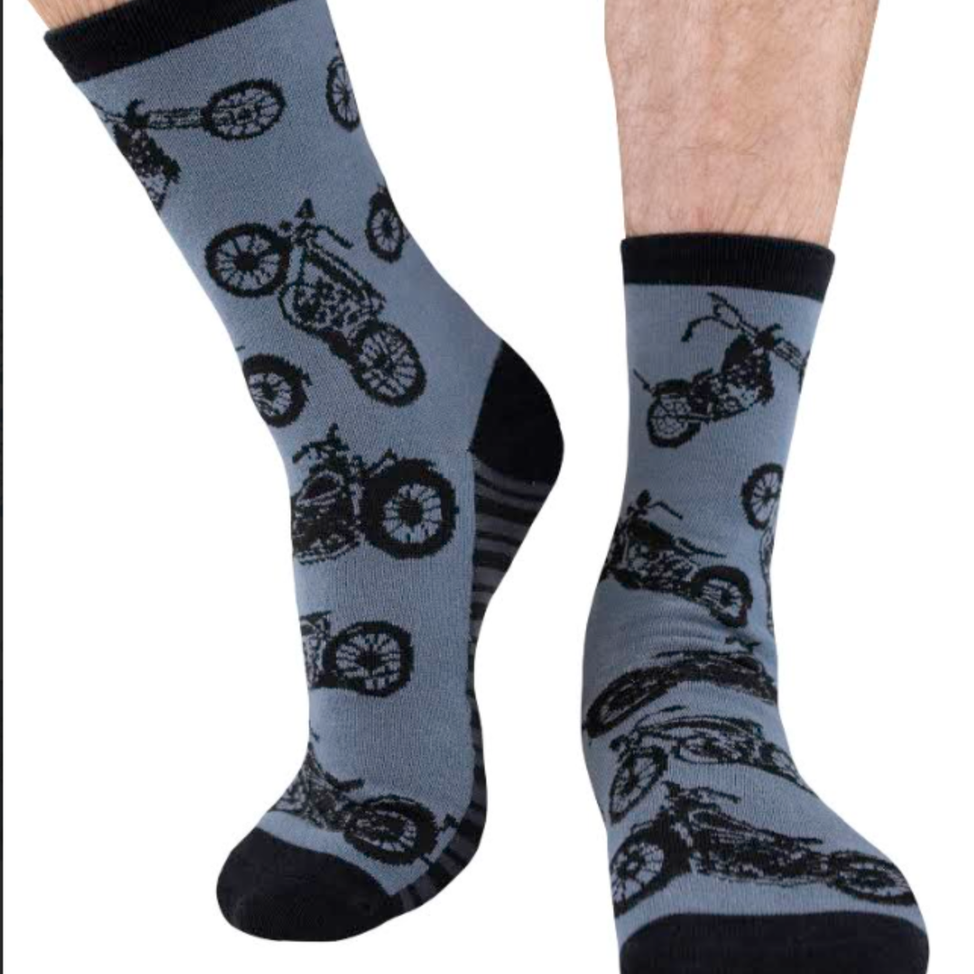 A pair of crew socks worn on feet, featuring a black motorcycle pattern on a light blue-gray background with black cuffs, heels, and toes.
