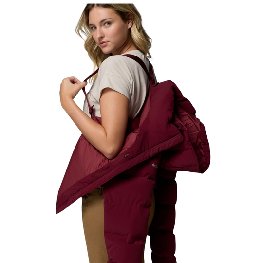 Woman wearing Columbia Women's Amaze Puff Hooded Jacket - Rich Wine on a plain white background. Showing off the suspender function. 