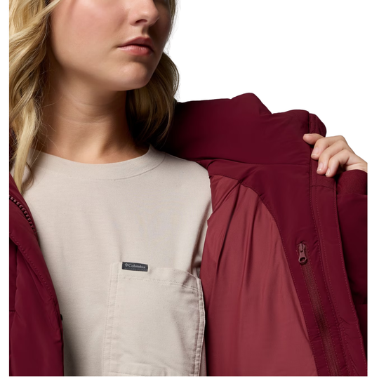 A close-up of a woman wearing a burgundy hooded jacket over a light beige top, with the jacket's front zipper and chest pocket visible against a plain white background.