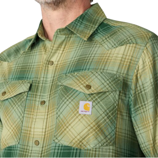 Man wearing Carhartt Men's Montana Rugged Flex Relaxed Fit Lightweight Long Sleeve Plaid Shirt - Faded Fatigue on a plain white background. Zoomed into Carhartt logo and button up.
