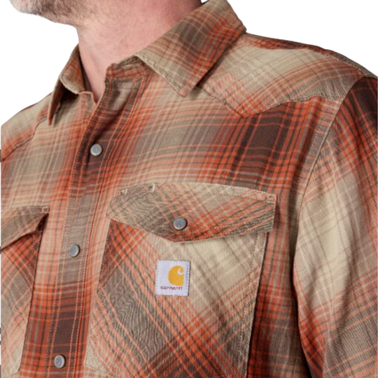 Man wearing Carhartt Men's Montana Rugged Flex Relaxed Fit Lightweight Long Sleeve Plaid Shirt - Dark Clove on a plain white background. Zoomed into the Carhartt logo and button up.