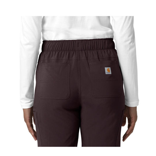 Rear view of a person wearing dark brown Carhartt scrub pants with an elastic waistband, two large back pockets, and a small Carhartt logo patch on the right pocket, paired with a white long-sleeve top on a white background.