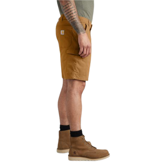 Side view of a person wearing Carhartt work shorts in a warm tan/camel color, paired with brown boots and black socks, against a plain white background.