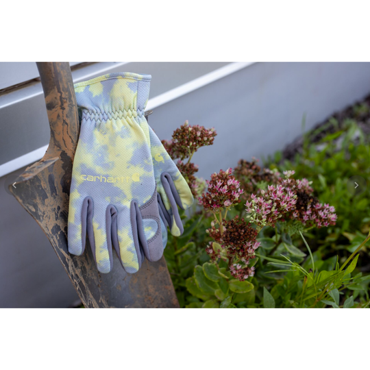 A pair of Carhartt work glove shown from the back, featuring a light blue and cream tie-dye pattern on the back with solid gray palm and finger backs, and the Carhartt logo printed on the gloves.