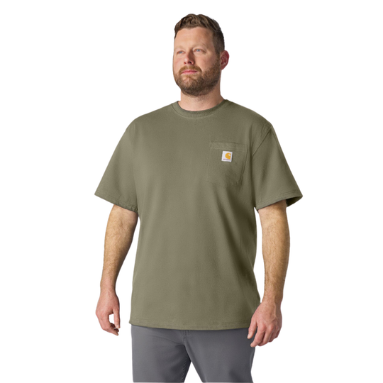A man wearing a short-sleeve crewneck pocket t-shirt in olive green with a small Carhartt logo patch on the chest pocket, paired with gray pants, against a plain white background.