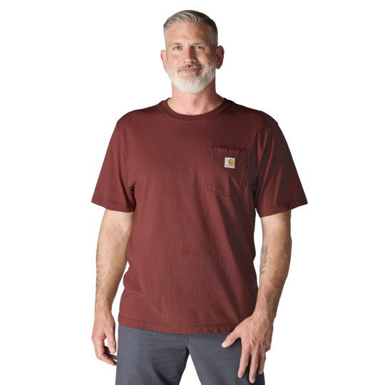 A man wearing a short-sleeve maroon work shirt with a chest pocket and a small Carhartt logo patch, paired with gray pants, against a plain white background.