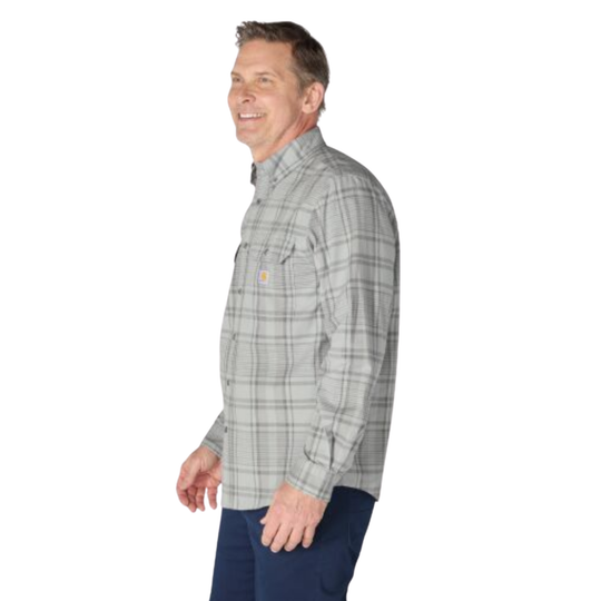 A man wearing a light gray and white plaid long-sleeve button-up shirt with a small yellow Carhartt logo on the chest pocket, paired with dark blue jeans, shown from a side profile against a white background.
