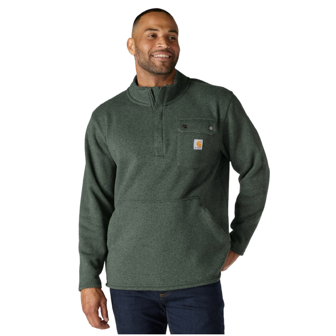 A man wearing a dark green heathered quarter-zip pullover sweater with a small Carhartt logo patch on the chest pocket, paired with dark blue jeans, against a plain white background.