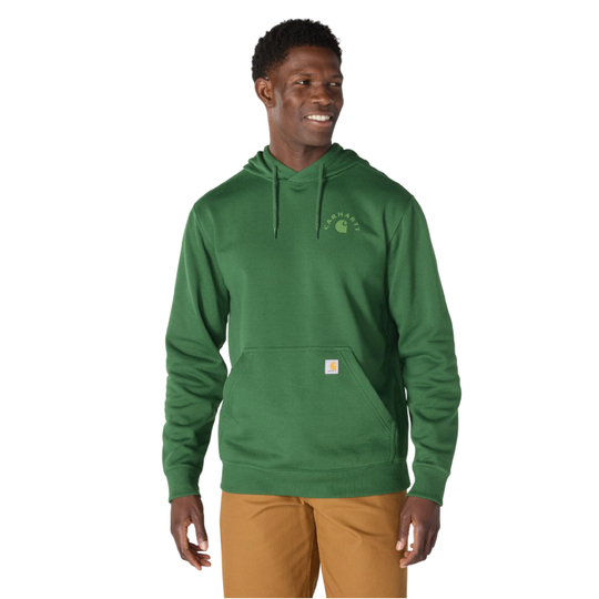 A man wearing a green Carhartt pullover hoodie with a small embroidered Carhartt logo on the left chest and a small orange brand tab on the front pocket, paired with tan pants, against a plain white background.