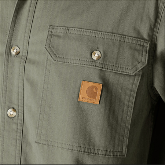 Close-up of an olive green Carhartt button-up shirt showing the chest pocket with a brown leather Carhartt logo patch.